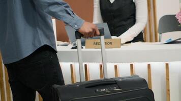 invitado de viaje con carretilla pantalones a hotel, recepción acceso llave tarjeta a recepción después largo vuelo. africano americano turista en vacaciones a cinco estrella fiesta complejo. cerca arriba. Mano disparo. foto