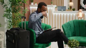 Hotel guest browsing page on tablet and enjoying cup of coffee whel he waits on room reservation, relaxing in lounge area and receiving luxurious services. Man traveller checking gadget. photo