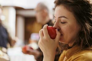 Woman smelling organic locally grown apples in zero waste supermarket while vendor talks with customer in blurry background. Client seeing if eco friendly local neighborhood shop fruits are fresh photo