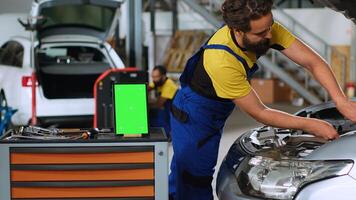 panorámica Disparo de croma llave tableta en garaje espacio de trabajo sentado en trabajo banco. Bosquejo dispositivo en coche Servicio siguiente a profesional herramientas con reparadores en antecedentes reacondicionamiento dañado vehículos foto