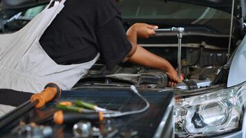 Trained technician in garage using torque wrench to tighten bolts inside opened up vehicle, preparing to change oil. Auto repair shop professional doing checkup on car to prevent issues, close up shot photo