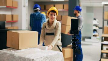 Supervisor recording advertisement video in depot, showing merchandise packages on social media app. Warehouse employee using smartphone to film PR ad, storage room racks. photo