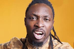 Portrait of dissatisfied worker having nervous expression on face while standing in studio over yellow background. Upset frustrated african american man feeling angry and furious. Mental breakdown photo