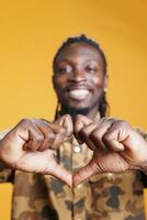 Lovely african american man making romantic gesture, doing heart shape with hands in studio over yellow background. Cheerful positive person showing affection and emotion, doing love sign photo