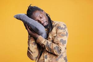 African american man putting head on comfortable pillow to sleep and take nap. Exhausted person trying to get rest after passing bedtime, sleeping in studio over yellow background. photo