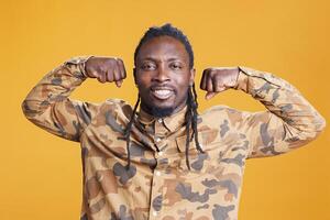 African american man flexing triceps strength before workout training in studio over yellow background. Confident athletic person posing to show biceps, muscular body from fitness photo