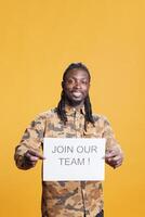 African american hr recruiter holding job offer sign, hiring candidate for business career opportunity standing in studio over yellow background. Advertisement with job application photo