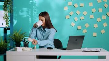 Office clerk enjoying cup of coffee while receiving important telephone call. Asian businesswoman talking over landline phone in colourful workplace over blue studio background photo