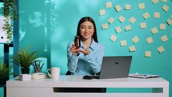 Cheerful affable asian medical saleswoman proudly presenting pill bottle, showing thumbs up sign. Office worker in modern relaxed colourful workplace over blue studio background photo