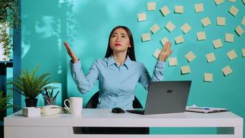 Worried employee praying looking up with hands raised toward the sky waiting for sign from divinity. Stressed asian woman at coloured office desk over blue studio background photo