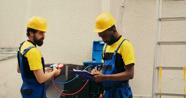 Adept repairmen working with manifold meters to check air conditioner refrigerant levels, writing result on clipboard. Proficient workers using barometer benchmarking outdoor hvac system tool photo