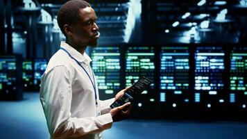 Experienced computer scientist maintenancing server rows delivering web content to online clients. African american supervisor using tablet to ensure critical systems functionality photo