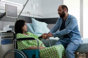 marido consolador embarazada mujer sentado en silla de ruedas, que se discute acerca de paternidad antes de cesariano cirugía. joven padres esperando para parto a maternidad clínica. medicina concepto foto