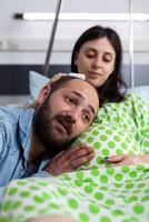 alegre futuro padre en pie con cabeza en mujer barriga, hablando con niño antes de cesariano cirugía en hospital pabellón. embarazada paciente preparando a entrega niño en maternidad instalaciones foto