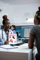 Cardiologist showing heart chart on tablet to patient during checkup appointment. Cardiac doctor specialist in modern clinic office presenting diagnostic and treatment information to woman photo