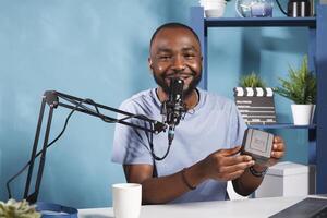 sonriente hombre de influencia transmisión regalar para social medios de comunicación y Hablando en micrófono retrato. africano americano vlogger grabación producto revisión y márketing vídeo para web Blog y mirando a cámara foto