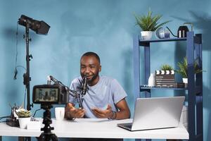 Blogger using camera and microphone for live streaming on social media channel. African american video vlogger creating digital content with professional equipment in studio photo