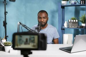 African american blogger recording video with professional camera in home studio. Vlogger speaking in microphone while live streaming and creating digital content for internet channel photo