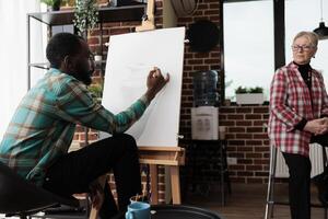 Young focused African American guy learning to draw with teacher, male student sitting at easel in classroom sketching simple object with pencil, taking up art classes. Drawing and selfexpression photo