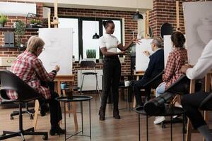 Young friendly African American woman art instructor standing in classroom communicating with student during group drawing workshop. Teaching beginning drawing classes for adults photo