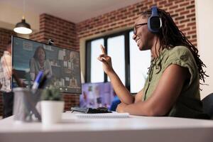 African american startup employee in video conference with team making ok hand sign while talking and smiling. Freelancer with headphones in internet call gesturing while talking with manager. photo