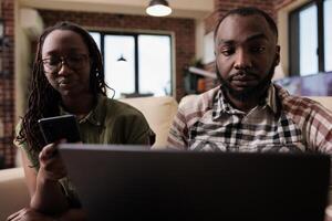 Couple having communication problems not talking to each other and using digital devices ignoring each other. Woman browsing social media on smartphone while man is working on laptop. photo