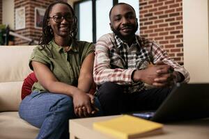 African american couple living together binging online series on laptop looking at screen in home living room. Happy woman and boyfriend watching entertainment show on portable computer. photo