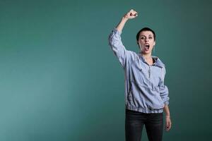 Excited woman celebrating good scoring of soccer championship, cheering football team while standing in studio with isolated background. Happy female raising hands after winning the competition photo