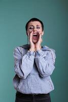 Portrait of stressed angry caucasian female having mental breakdown in studio standing over isolated background. Unhappy agressive woman screeming while looking at camera, negative facial expression photo