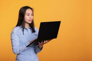 Asian woman using digital device browsing webpages on internet, searching information for research project. Young adult using laptop computer to navigate on social media. Remote work concept photo