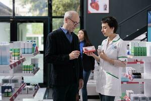 Elderly man buying supplements and getting heart health advice from pharmacist in drugstore. Pharmaceutical specialist explaining senior person differences between vitamin complex photo