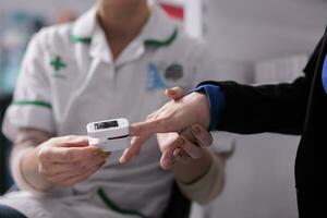 Apothecary worker putting pulse oximeter on patient finger for cardiology disease diagnosis. Pharmaceutical assistant examining drugstore client heart health and measuring oxygen level in blood photo