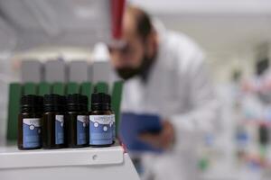 Selective focus of essential oil on pharmacy shelves is ready to be buy by client, man doing inventory in background. Drugstore is a vital resource for the community, providing access health services. photo