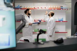 Two men pharmacists doing medicaments inventory checking pills packages, writing drugs information on papers. Pharmacy is a reliable and convenient location for filling prescription medication photo