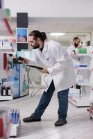 Drugstore worker looking at drugs packages while scanning supplements products using store scanner typing bar code on tablet. Pharmacist checks the expiration date on the medication boxes in pharmacy photo