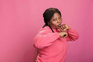 Aggressive model clenching fists and showing raised knuckles on camera in studio, feeling angry and doing air punches. Furious african american woman preparing to fight doing combat demonstration. photo