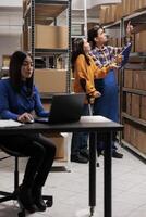 Warehouse asian man and woman managers picking order and taking parcel from shelf. Storehouse employee and postal delivery operator managing goods quality control in storage room photo