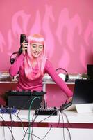 asiático artista teniendo divertido mientras ejecutando electrónica música en noche club jugando canción utilizando profesional tocadiscos. mujer en pie a DJ mesa bailando mientras celebrando techno álbum con aficionados foto