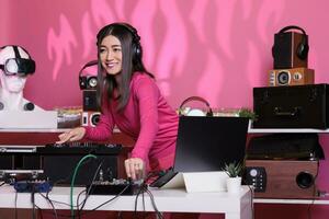 Cheerful performer playing electronic music using professional mixer console while standing at dj table in studio over pink background. Artist doing performance at nightclub with audio equipment photo