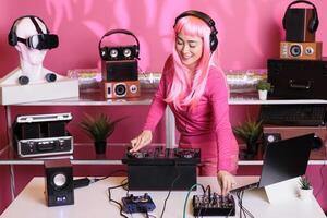 Musical artist with pink hair playing techno song at professional mixer console, enjoying performing music in club during night time. Asian performer mixing sounds in studio with isolated background photo