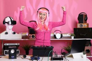 ejecutante con rosado pelo ejecutando techno música utilizando DJ mezclador consola disfrutando a jugar canción con aficionados, teniendo divertido en club a noche. artista haciendo actuación con profesional audio equipo foto