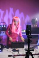 Cheerful artist performing electronic song at turntables while filming music process with phone camera in studio. Dj woman doing performance at nightclub with professional audio equipment photo