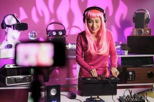 Cheerful artist standing at dj table in night club performing techno song using mixer console while filming music session with professional camera. Woman posting performance video on her channel photo