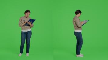 Confident woman looking at clipboard files on full body greenscreen, taking notes on papers and working on analysis. Female model writing information on documents in studio. photo