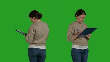 Close up of casual adult analyzing clipboard papers in studio, standing on greenscreen background. Positive woman taking notes on files writing information on documents, working on analysis. photo