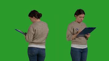 Close up of casual adult analyzing clipboard papers in studio, standing on greenscreen background. Positive woman taking notes on files writing information on documents, working on analysis. photo