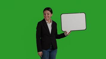 Front view of business manager holding speech bubble on camera, showing isolated cardboard icon over greenscreen backdrop. Woman in suit using carton board with blank copyspace in studio. photo