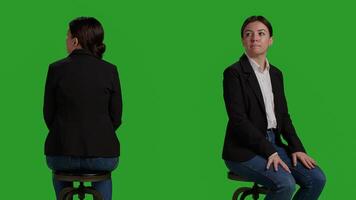 Close up of company worker waiting on chair before attending business meeting, sitting in studio with greenscreen background. Woman dressed in office suit working as employee or manager. photo