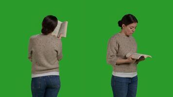 Young person with action book reading in studio, enjoying novel chapter with story. Caucasian woman standing over isolated greenscreen backdrop, read tale on camera as leisure activity. photo