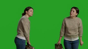 Young woman carrying vintage briefcase in front of camera, holding suitcase in studio before leaving on journey. Cheerful person acting optimistic and having travel bags or luggage over greenscreen. photo